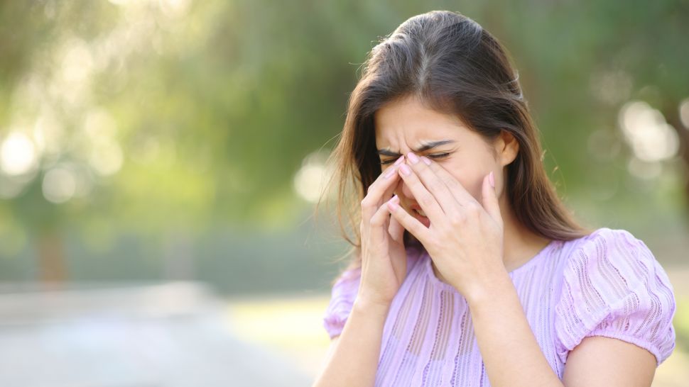 Жена с алергия към полени, кихаща и търкаща носа си на открито